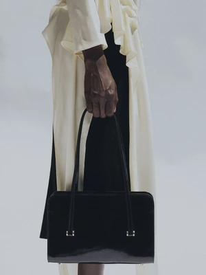 Close-up of a person holding a structured black leather handbag against a plain grey background