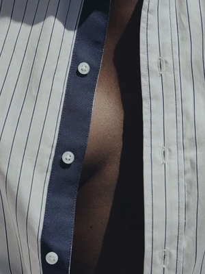 Extreme close-up macro shot of a blue and white pinstriped button-down shirt worn open over dark skin.