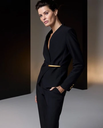 Elegant woman in a black pantsuit poses in a photo studio with modern background, showcasing fashion and style in a chic, minimalist aesthetic.