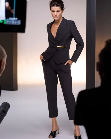 Model in a black suit standing in a studio with crew members visible in the foreground for Donna Karan In Women We Trust 2025 campaign