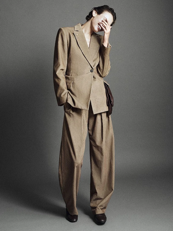 Model laughing while wearing a tailored camel-coloured suit against a grey studio backdrop