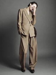 Model laughing while wearing a tailored camel-coloured suit against a grey studio backdrop