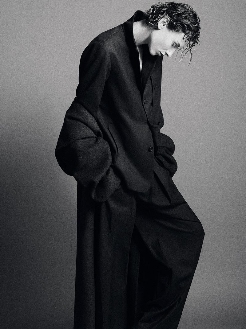 Model in black tailored coat and trousers against a grey studio backdrop captured by Su Mustecaplioglu for Kallmeyer.