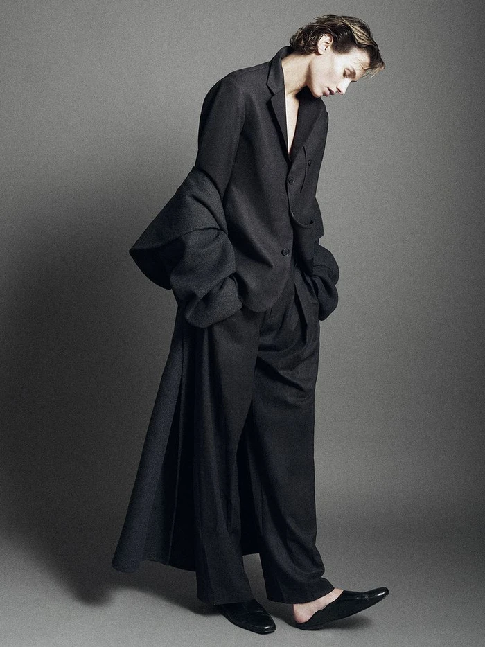 Model standing against grey studio background wearing dark oversized blazer and trousers from Kallmeyer