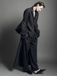 Model standing against grey studio background wearing dark oversized blazer and trousers from Kallmeyer