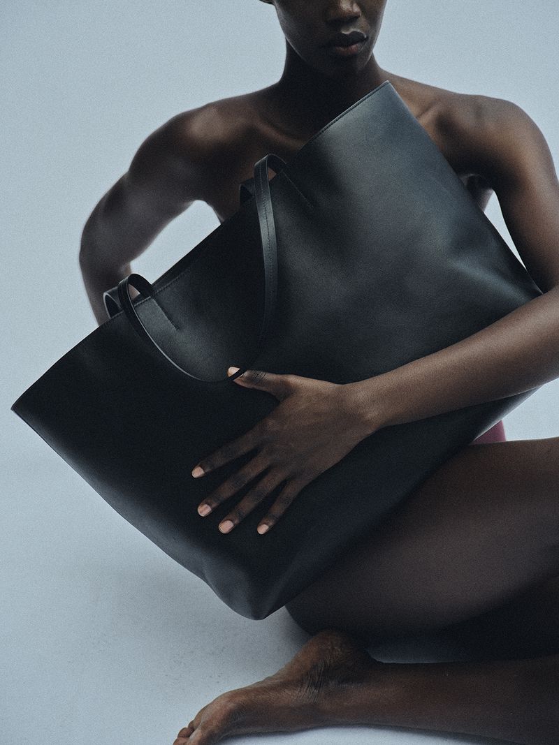 Model holding a large black leather tote bag against a neutral background for Kallmeyer Magazine Hold Close