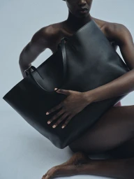 Model holding a large black leather tote bag against a neutral background for Kallmeyer Magazine Hold Close