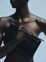 Model holding a black leather clutch bag against a soft blue background