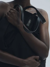 Close-up of a person holding a black handbag against a neutral background for Kallmeyer Magazine Hold Close.