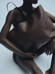 Model holding a large brown leather tote bag against a pale neutral background