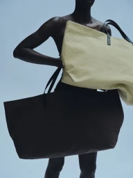 Model holding two large canvas tote bags against a light blue background for Kallmeyer Magazine