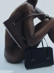 Model holding dark leather handbags against a neutral studio background for Kallmeyer Magazine Hold Close project