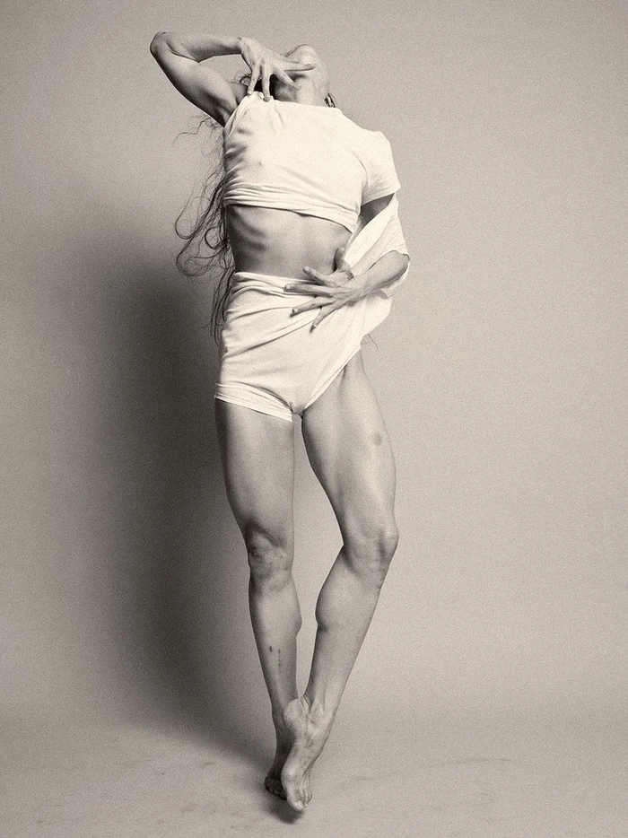Model in white t shirt and white shorts posing dynamically against a neutral grey seamless background.