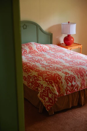 A made bed with red patterned duvet, green headboard, and bedside table with a red lamp