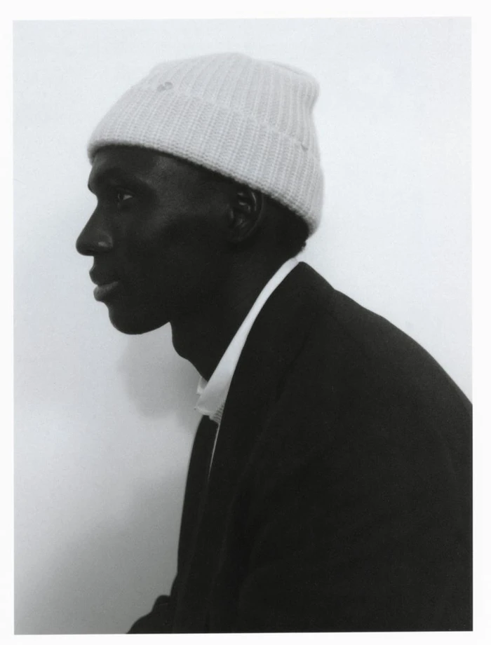 Profile portrait of a Black man wearing a white beanie and dark jacket against a plain white background.