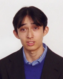Portrait of a man wearing a blue knit sweater and dark blazer against a plain background for Auralee.