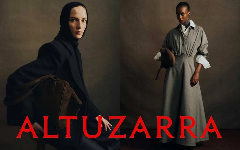 Two models showcasing Altuzarra Fall 2026 fashion looks against a dark textured studio backdrop with red brand lettering.