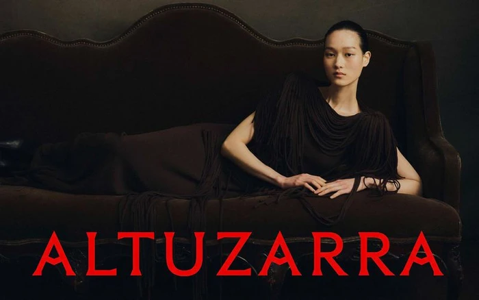 Model reclining on a dark velvet vintage sofa wearing a fringed dark dress for Altuzarra Fall 2026 collection.