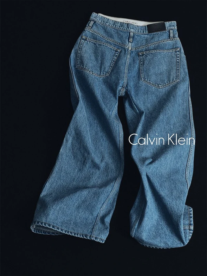 Blue denim jeans laid flat against a black background with Calvin Klein logo typography visible