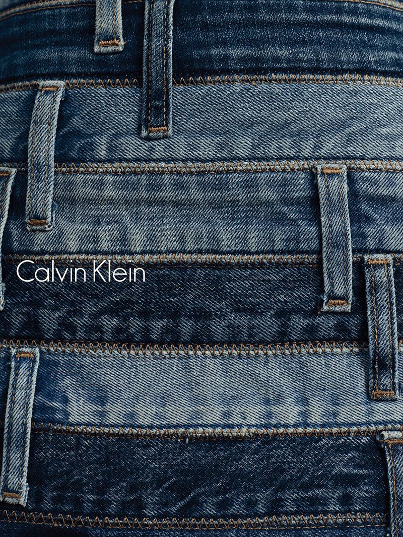 Close-up macro shot of layered blue denim waistbands with belt loops and topstitching, featuring the Calvin Klein logo