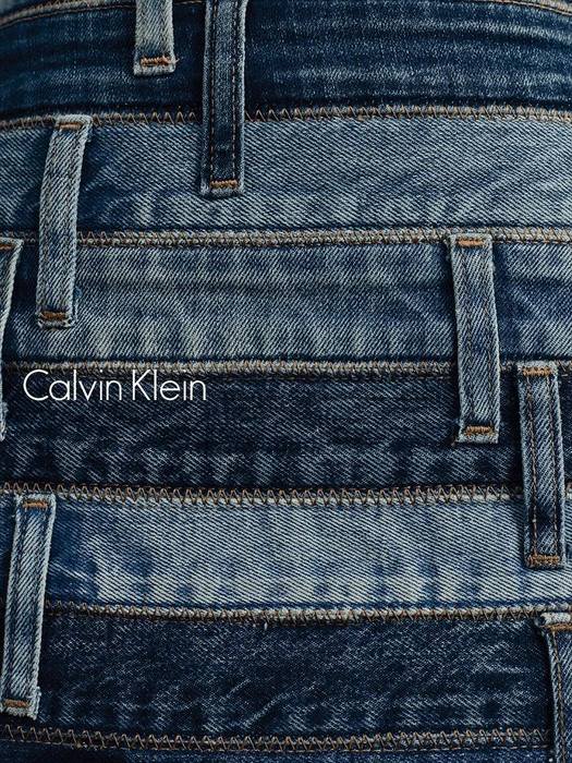 Close-up macro shot of layered blue denim waistbands with belt loops and topstitching, featuring the Calvin Klein logo