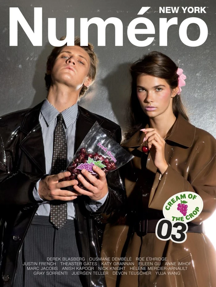 Two models holding a bag of grapes and cherries against a dark metallic wall for Numéro New York magazine.