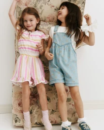 Two young girls laughing while posing against a floral upholstered armchair in Country Road children's fashion campaign