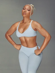 Megan Thee Stallion in a light blue sports bra and matching leggings posing against a grey seamless studio backdrop for Gymshark.