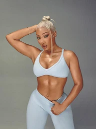 Megan Thee Stallion wearing light blue activewear set with blonde braided hair in high bun against grey background for Gymshark