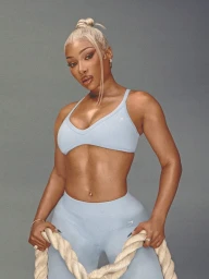 Megan Thee Stallion in a light blue sports bra and leggings holding a thick rope against a grey background for Gymshark.