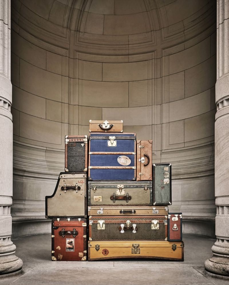 Stacked antique luggage in front of an archway featuring column pillars, vintage aesthetic and muted neutral color palette.