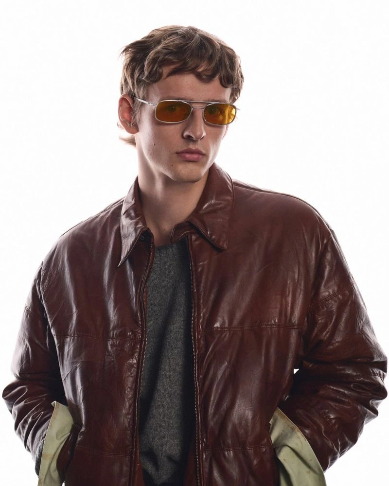 Model wearing tinted sunglasses and a brown leather jacket against a plain white background for the Prada eyewear campaign