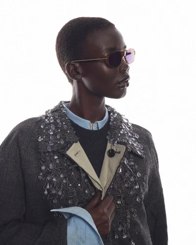 Model Achol Ayor wearing Prada sunglasses and embellished dark coat against a white background