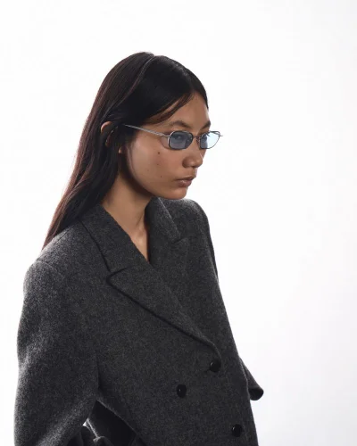 Model wearing tinted sunglasses and a dark grey wool blazer against a white seamless background