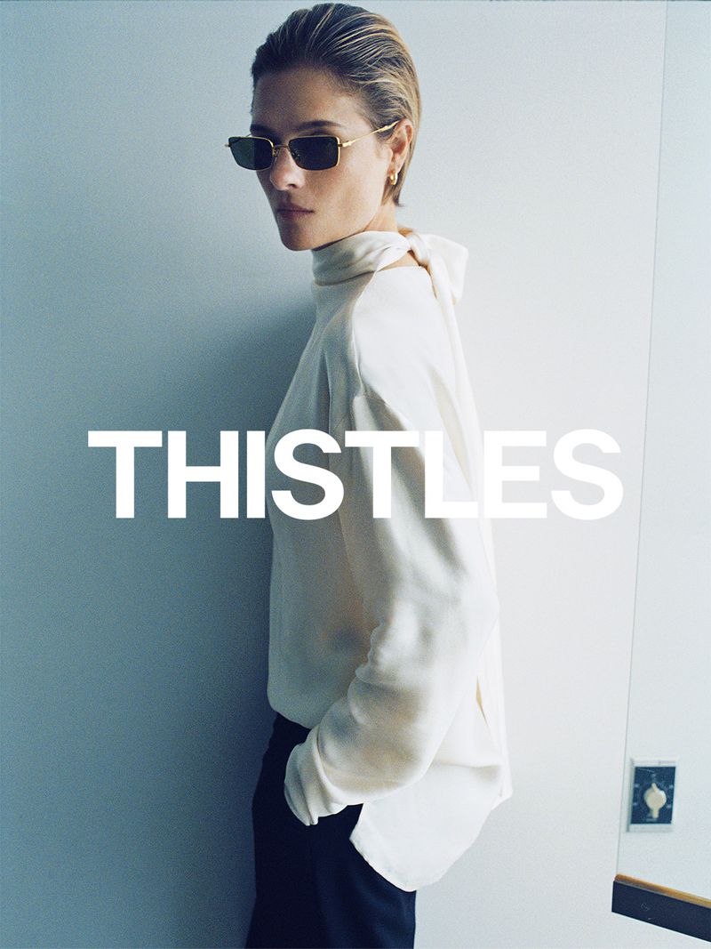 Model Louisa Jacobson wearing sunglasses and a white top against a wall for Thistles AW26 campaign