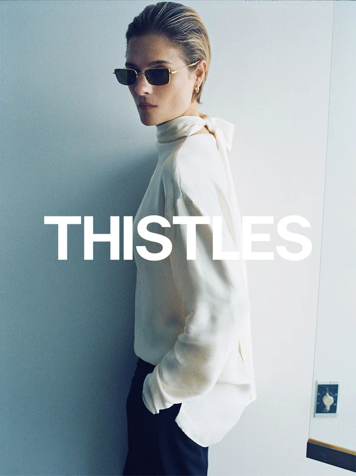 Model Louisa Jacobson wearing sunglasses and a white top against a wall for Thistles AW26 campaign
