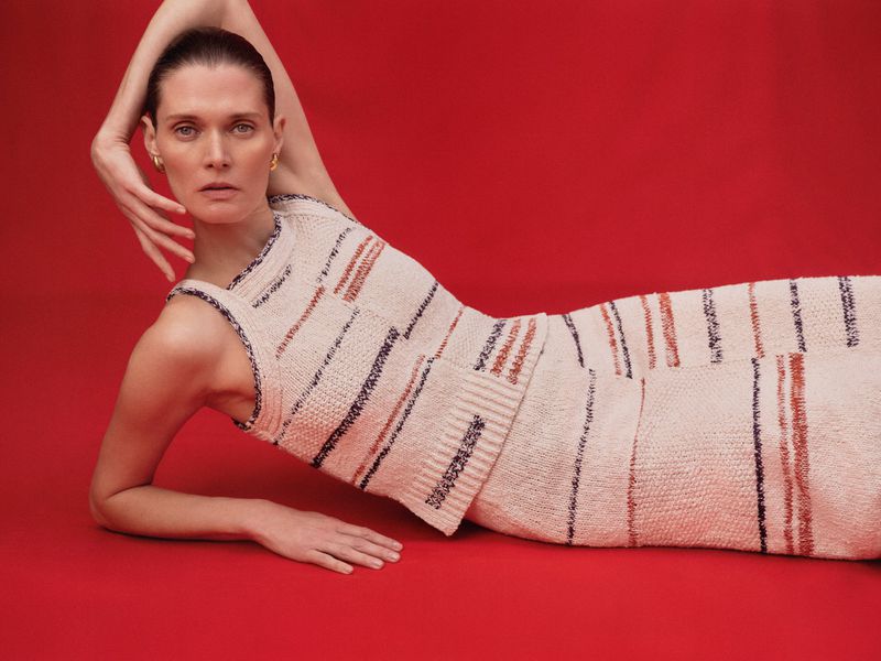 Adult woman in a light patterned top and skirt lies on a red surface, looking at the camera with a neutral expression.