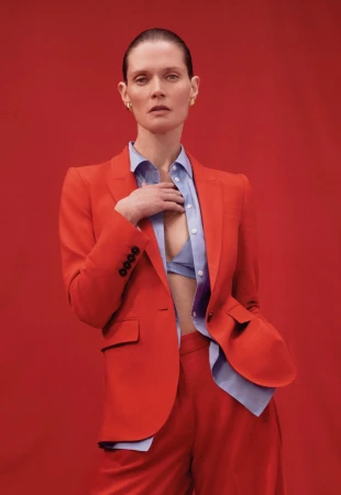 Fashionable woman with a red suit and blue shirt poses in a portrait against a matching red backdrop for a studio fashion shoot.