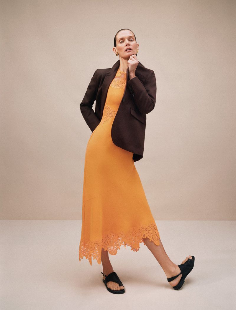 Model Malgosia Bela wearing an orange dress and dark blazer against a seamless studio background for ME+EM.