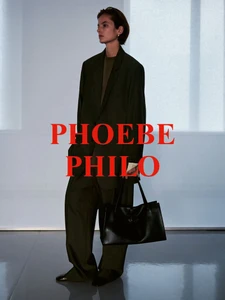 Model wearing a dark green oversized blazer and matching trousers, holding a black leather tote bag in a studio setting.