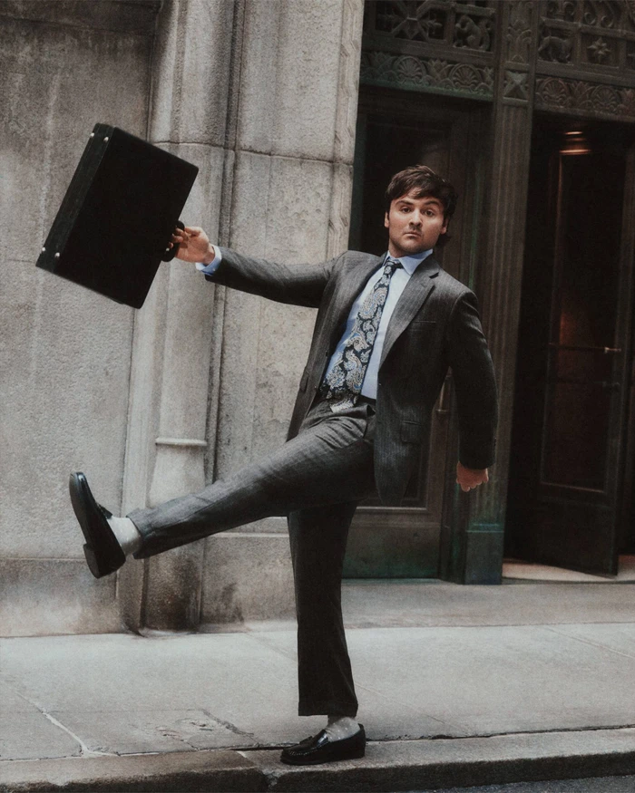 Man in a grey suit holding a black briefcase and stepping high outside a stone building entrance