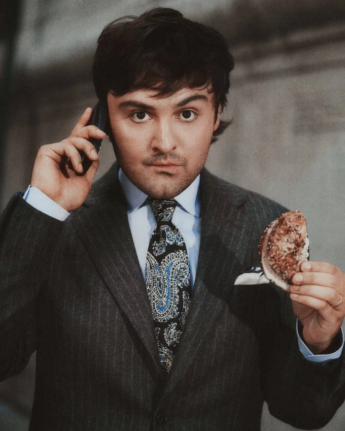 Man in a pinstripe suit holding a phone to his ear and a bagel in his hand for J. Crew