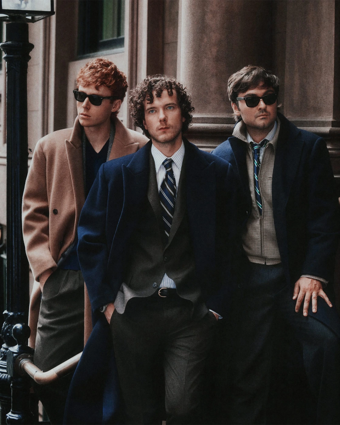 Three men in tailored coats and sunglasses posing outdoors by stone architecture for J. Crew Fall 2026 Ad Campaign