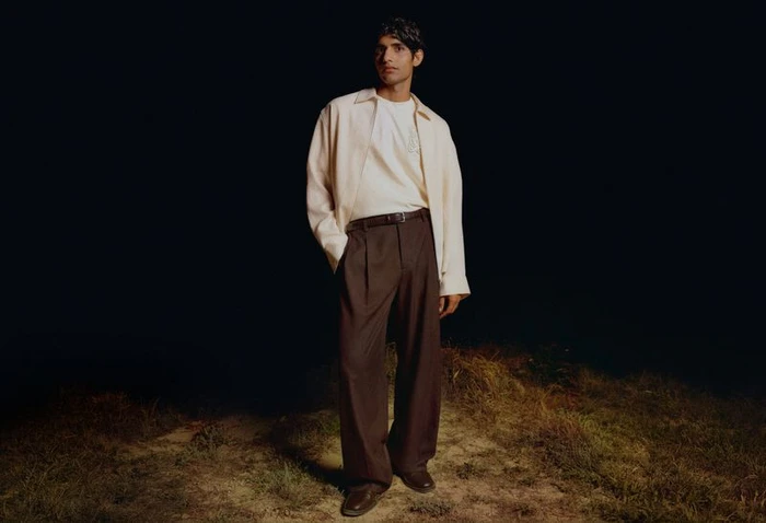 Model standing outdoors at night wearing a cream shirt and dark brown trousers for H&M Diwali Collection 2026.