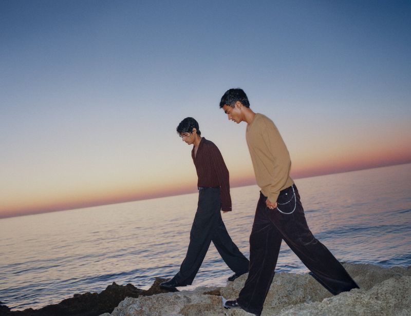 Two men walking along a rocky shoreline by the ocean at dusk for the H&M Diwali Collection 2026 campaign.