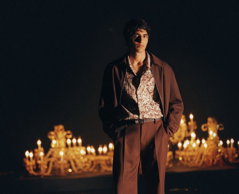Model wearing a brown jacket and patterned shirt with candles glowing in the background for H and M