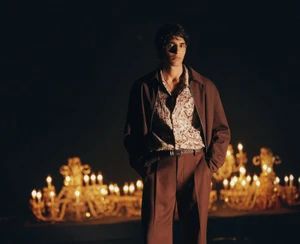 Model wearing a brown jacket and patterned shirt with candles glowing in the background for H and M