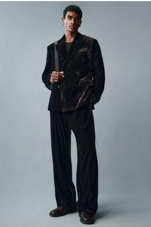 Man wearing a dark velvet double-breasted suit and trousers against a neutral grey studio background