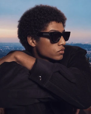 Man wearing dark sunglasses and black jacket against an outdoor dusk skyline background for Amiri 2026 Winter Capsule.