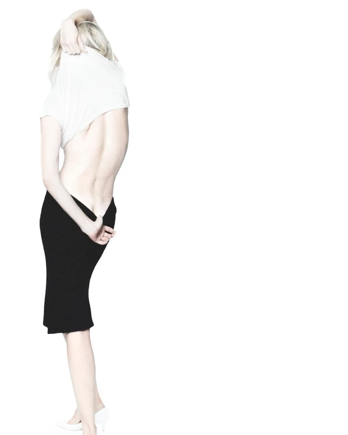 Dree Hemingway removing a white top wearing a black skirt against a seamless white background